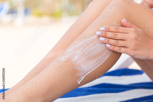 Young woman is relaxing on the sunbed at the beach and applying sun lotion on her leg with her hand