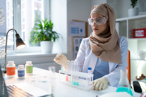 Busy chemist wearing gloves and glasses sitting and working