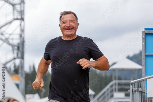 Smiling senior man running towards camera in rainy weather