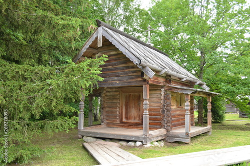 Old wooden house against the background of green grass and trees in the museum of wooden architecture.