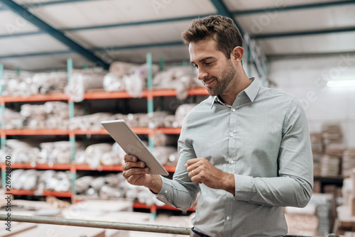 Smiling manager standing in his warehouse using a digital tablet