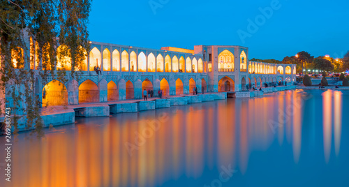 People resting in the ancient Khaju Bridge at twilight blue hour - Isfahan, Iran