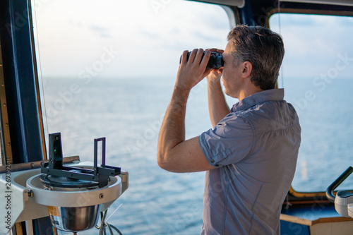 Navigational officer lookout on navigation watch looking through binoculars. Marine industry. COLREG collision regulations