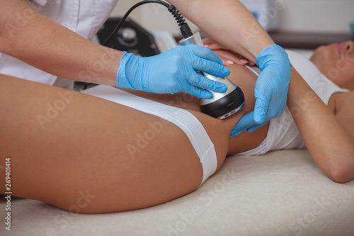 Cropped shot of a cosmetologist doing ultrasound cavitation procedure on the belly of a female client. Unrecognizable woman getting anti-fat treatment at beauty salon. Abdominal slimming concept