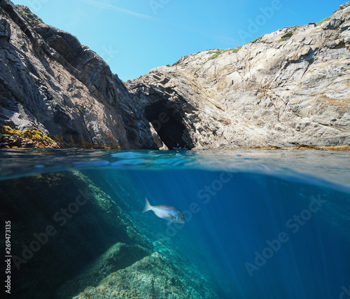 Rocky coastline with a natural arch and a fish underwater, Spain, Mediterranean, Costa Brava, Cap de Creus, Cueva del infierno, split view half over and under water