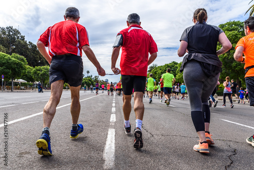 Valencia, Spain - May 19, 2019: Mature man blind runner and his companion joined by a cord to guide him during an amateur competition surrounded by other runners reaching the finish line.