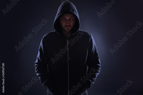 Mysterious man in hoodie on dark background. Dangerous criminal