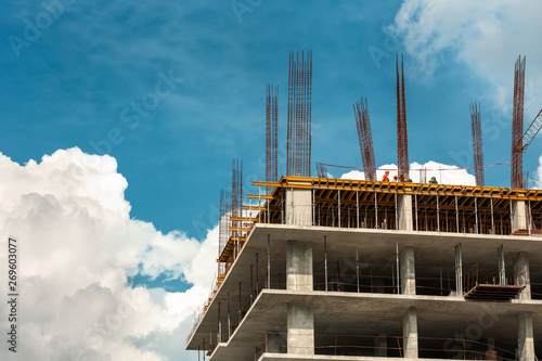 A building under construction with some small workers against sky. Concept: project, building, tower, business centre