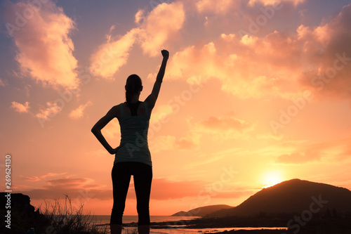 silhouette of young strong victorious woman with fist in the air at sunset