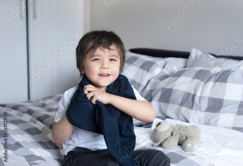 Cute boy learning how to put cloth on, 4 year old kid sitting in bed with teddy bear wearing school jumper,boy getting dressed and get ready for school, Child dressing uniform in bed room.