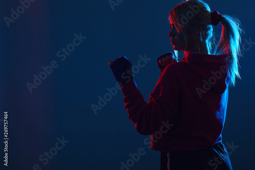 Silhouette of Female Muay Thai fighter with hairs tied in ponytail, standing in defensive stance at the corner over dark blue background with copy space
