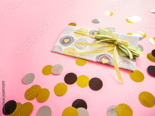 Design envelope with green ribbon on pink background. Birthday card with colorful confetti. Congratulations flatlay with gift certificate isolated on trendy backdrop. Holiday concept with top view
