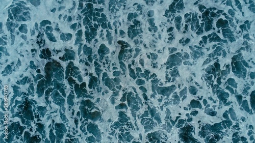 aerial drone image top looking down of surf waves rolling over a reef with white water break