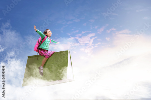 Asian cute girl with glasses and backpack sitting on the book with blue sky background