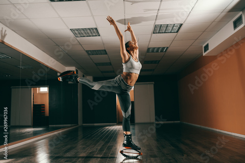 Beautiful fit Caucasian brunette in sportswear jumping on kangoo jumps footwear in gym.