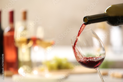 Pouring red wine from bottle into glass on blurred background. Space for text