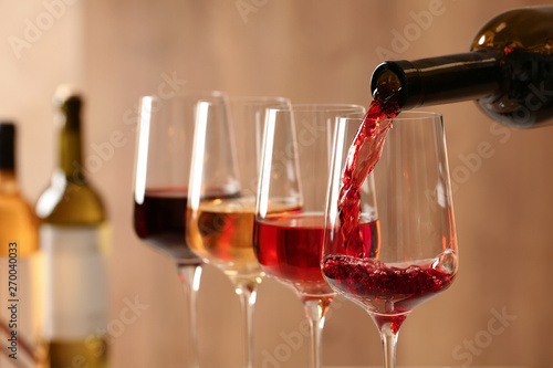 Pouring wine from bottle into glass on blurred background, closeup