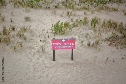 Tabliczka z napisem REZERWAT PRZYRODY WSTĘP WZBRONIONY stoi na piaszczystej wydmie
