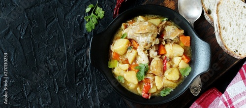 Chicken stew with potatoes and vegetables. in a black pan for serving dishes on a dark background surrounded by spices. meat and vegetables are pre-fried and then stewed. top view. copy space. 