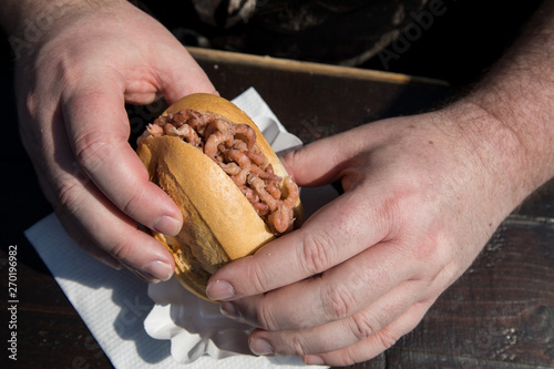 Mann isst Nordseekrabben Brötchen als Fischbrötchen auf Fischmarkt an Holztisch als schneller regionaler Imbiss