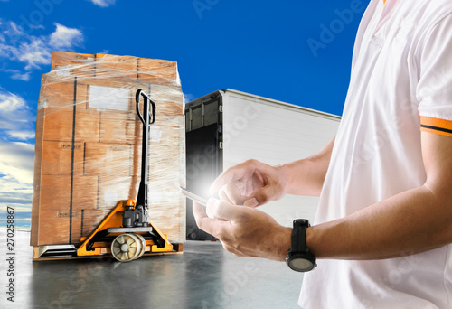 warehouse and transportation. shipper man hand holding smartphone his contact to customers. hand pallet truck with the shipment and truck docking at warehouse.