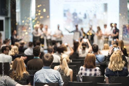 Young business team receiving award prize at best business project competition event. Business and entrepreneurship award ceremony theme. Focus on unrecognizable people in audience.