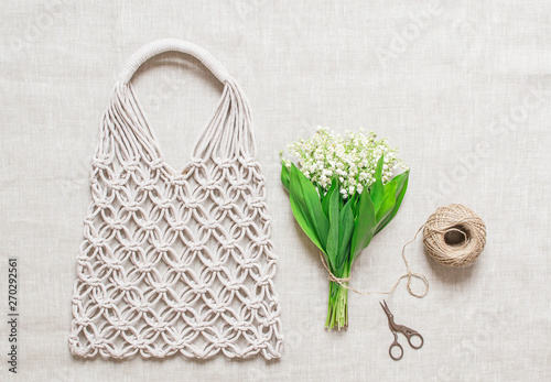 Handmade macrame bag on the linen background, ECO friendly. Embroidery. Modern summer concept. Lily of the valley bouquet 