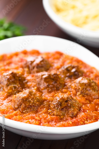 Homemade beef meatballs in fresh tomato sauce in bowl (Selective Focus, Focus on the front of the first two meatballs)