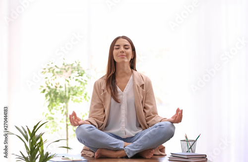 Young businesswoman meditating at workplace. Zen concept