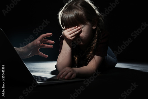 Stranger reaching frightened little child with laptop on dark background. Cyber danger