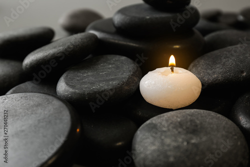 Small burning candle on beautiful spa stones, space for text