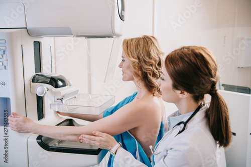 young radiographer standing near patient while making mammography test on x-ray machine