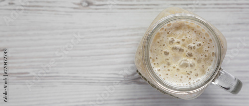 Banana smoothie in a glass jar over white wooden background, top view. Flat lay, overhead, from above. Copy space.