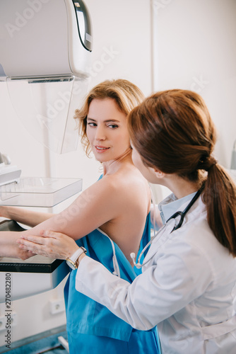 young doctor assisting patient while making mammography test on x-ray machine