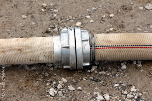 Heavily used large diameter fire hose connected with thick metal connection and enhanced with wire used to pump flood water from backyard surrounded with gravel and dirt on rainy spring day