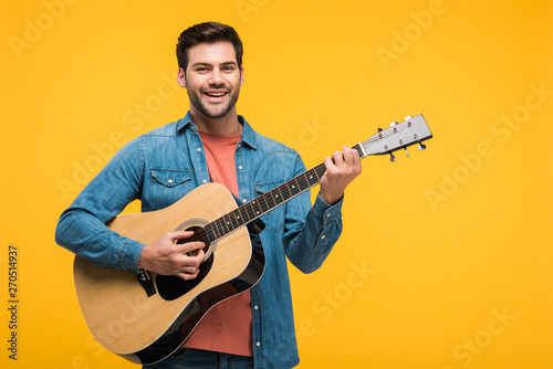 handsome smiling man playing acoustic guitar Isolated On yellow