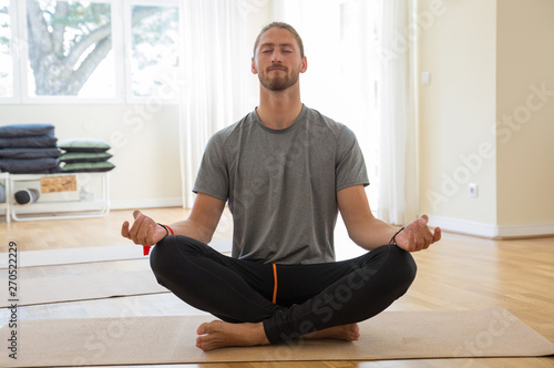 Man meditating and holding hands in mudra gesture in class. Handsome young guy practicing yoga and sitting with his legs crossed. Meditation and yoga class concept. Front view.