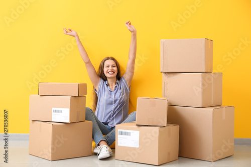 Young woman with many cardboard boxes near color wall