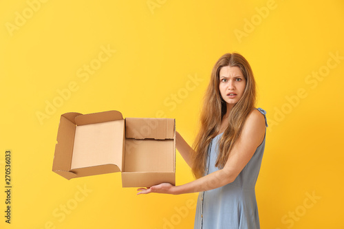 Displeased woman with empty cardboard box on color background
