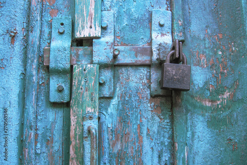 Vintage latch and closed padlock on weathered scratched wooden door. Concept of security and privacy protection. Textured grunge background