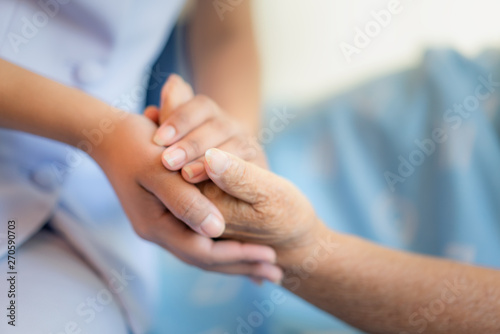 Nurse sitting on a hospital bed next to an older woman helping hands, care for the elderly concept