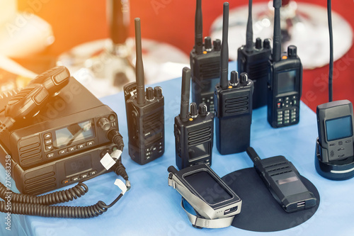 Many portable radio transceivers on table at technology exhibition. Different walkie-talkie radio set. Communication devices choice for military and civil use