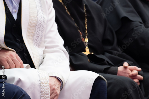 A Muslim mullah in white clothes and a Christian priest in a black cassock are sitting next to each other. The concept of religious cooperation, understanding, tolerance and friendship.