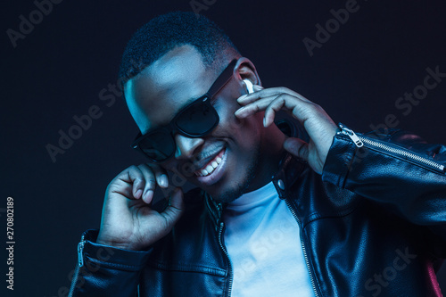 Smiling African male listening to music via wireless earphones at night