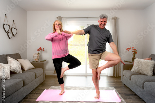 Middle aged retired couple practicing beginner starter yoga pose, fun fitness at home in living room