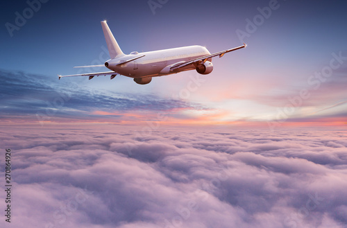 Commercial airplane jetliner flying above dramatic clouds in beautiful sunset light. Travel concept.