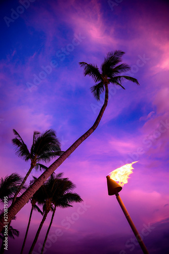 Tiki torch against colorful tropical sunset with palm trees