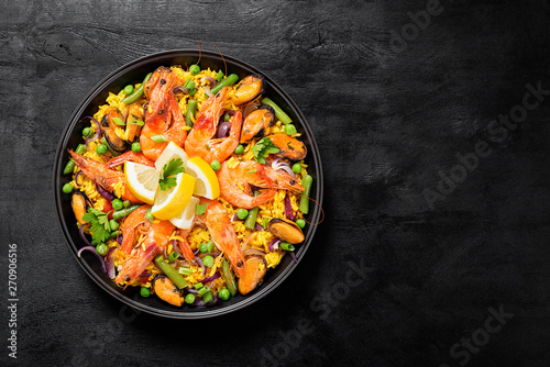 Traditional spanish seafood paella in the fry pan on a black wooden table, top view.