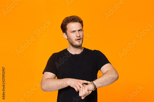 Studio shot of a bearded young man in black t-shirt pointing at the wristwatch.