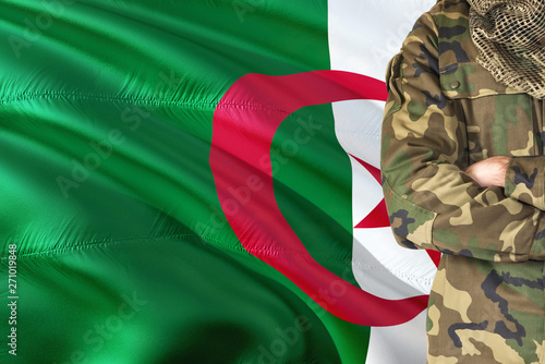 Crossed arms Algerian soldier with national waving flag on background - Algeria Military theme.